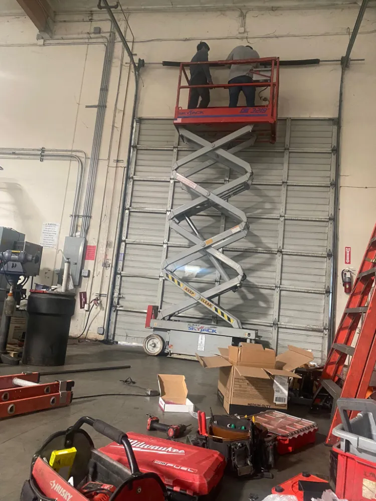 PLL technician on a scissor lift servicing a tall commercial garage door
