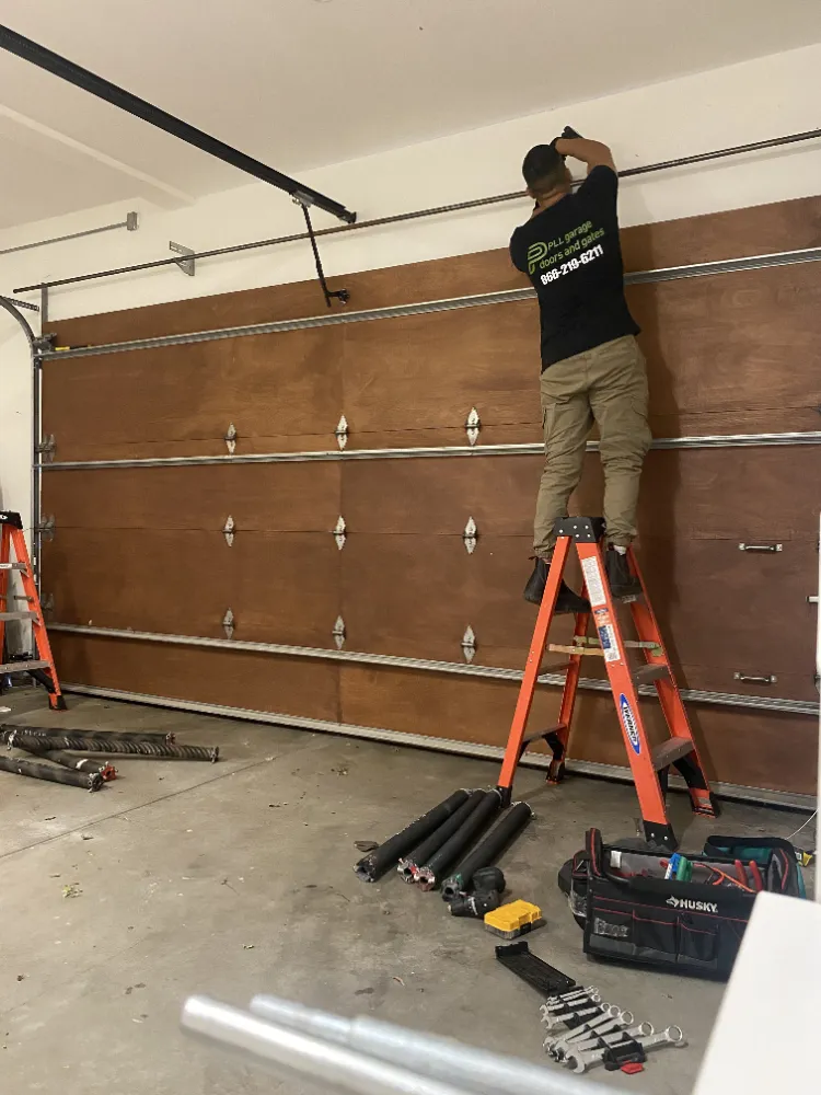 PLL technician installing a new garage door, with new springs and hardware ready on the floor